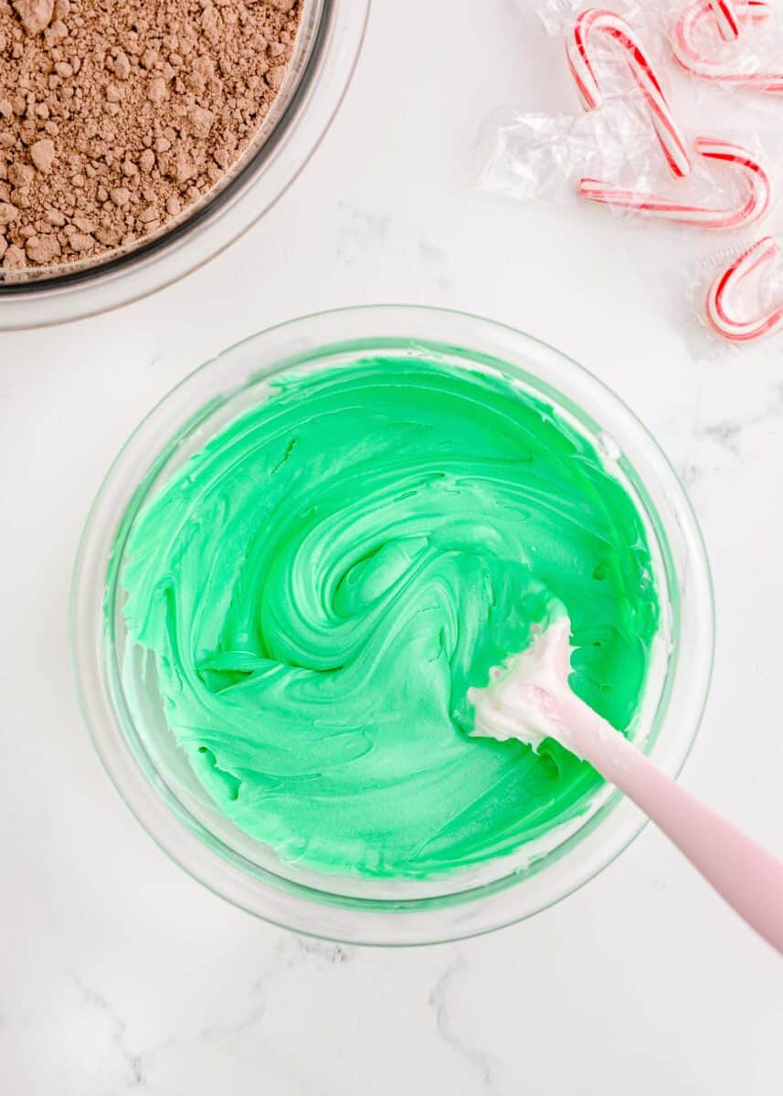 silicone spatula mixing together green frosting in a clear bowl