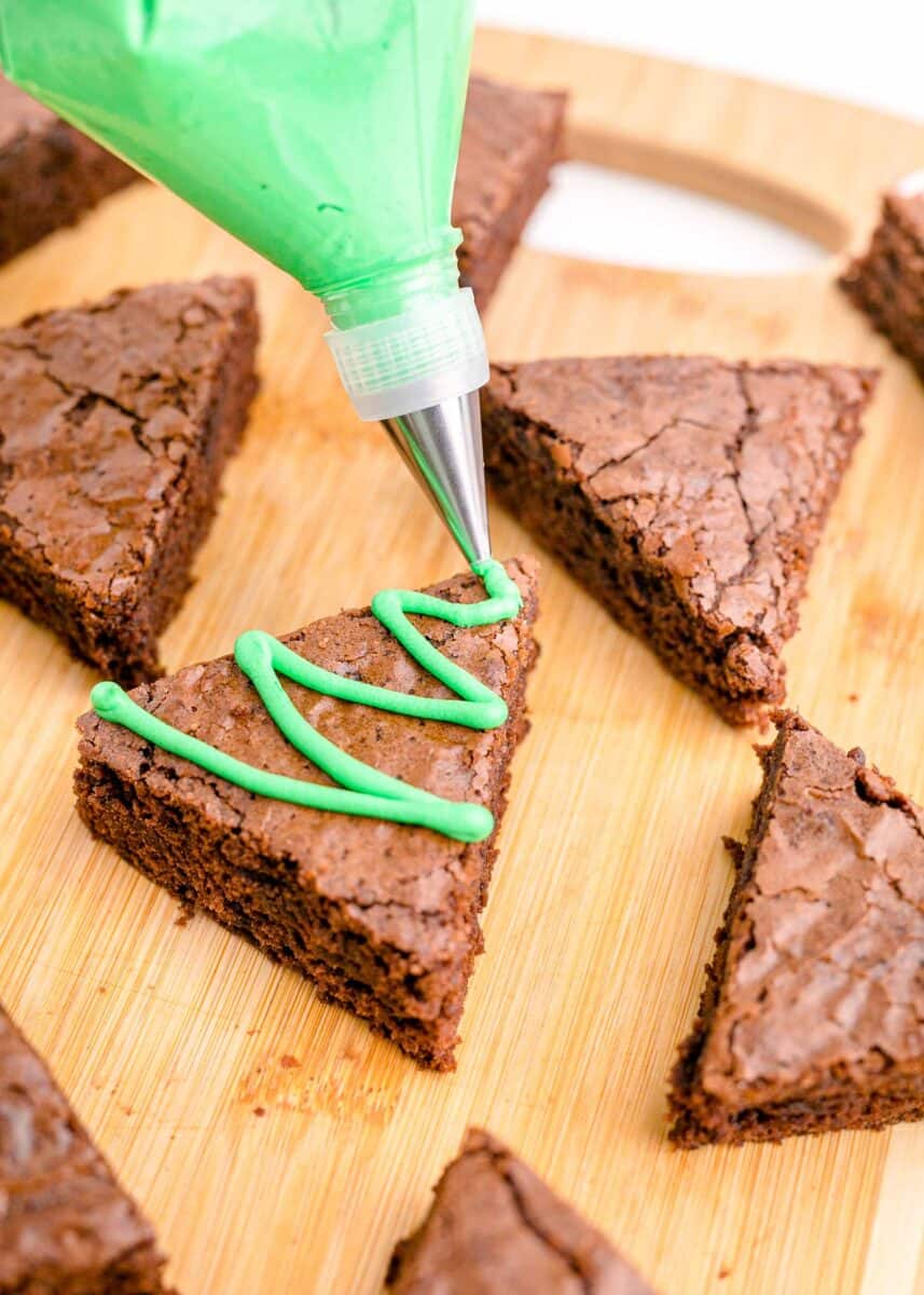 piping green frosting on top of brownie triangles