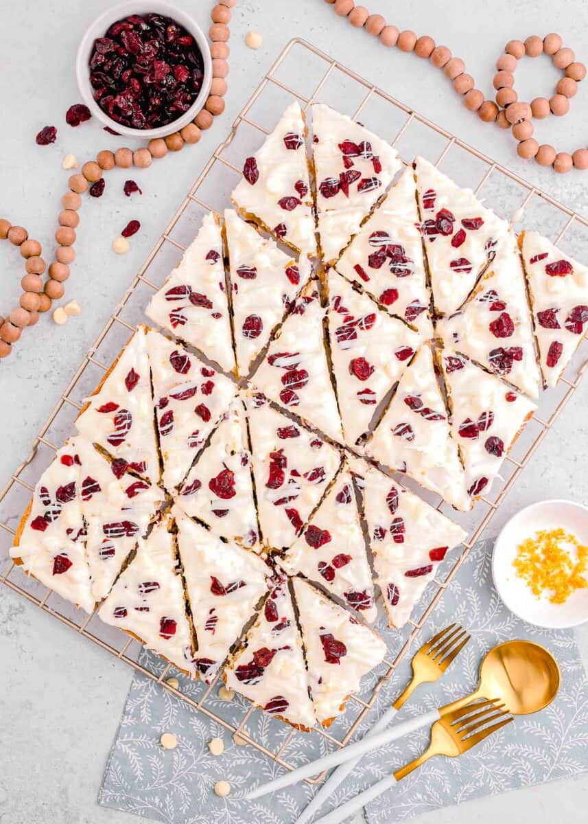 an entire sheet of cranberry bliss bars cut into triangles on a metal baking rack with a bead necklace around the tray