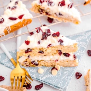 cranberry bliss bars on top of a blue floral napkin in front of metal baking rack with cranberry bliss bars on top