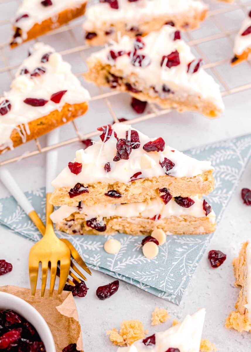 cranberry bliss bars on top of a blue floral napkin in front of metal baking rack with cranberry bliss bars on top