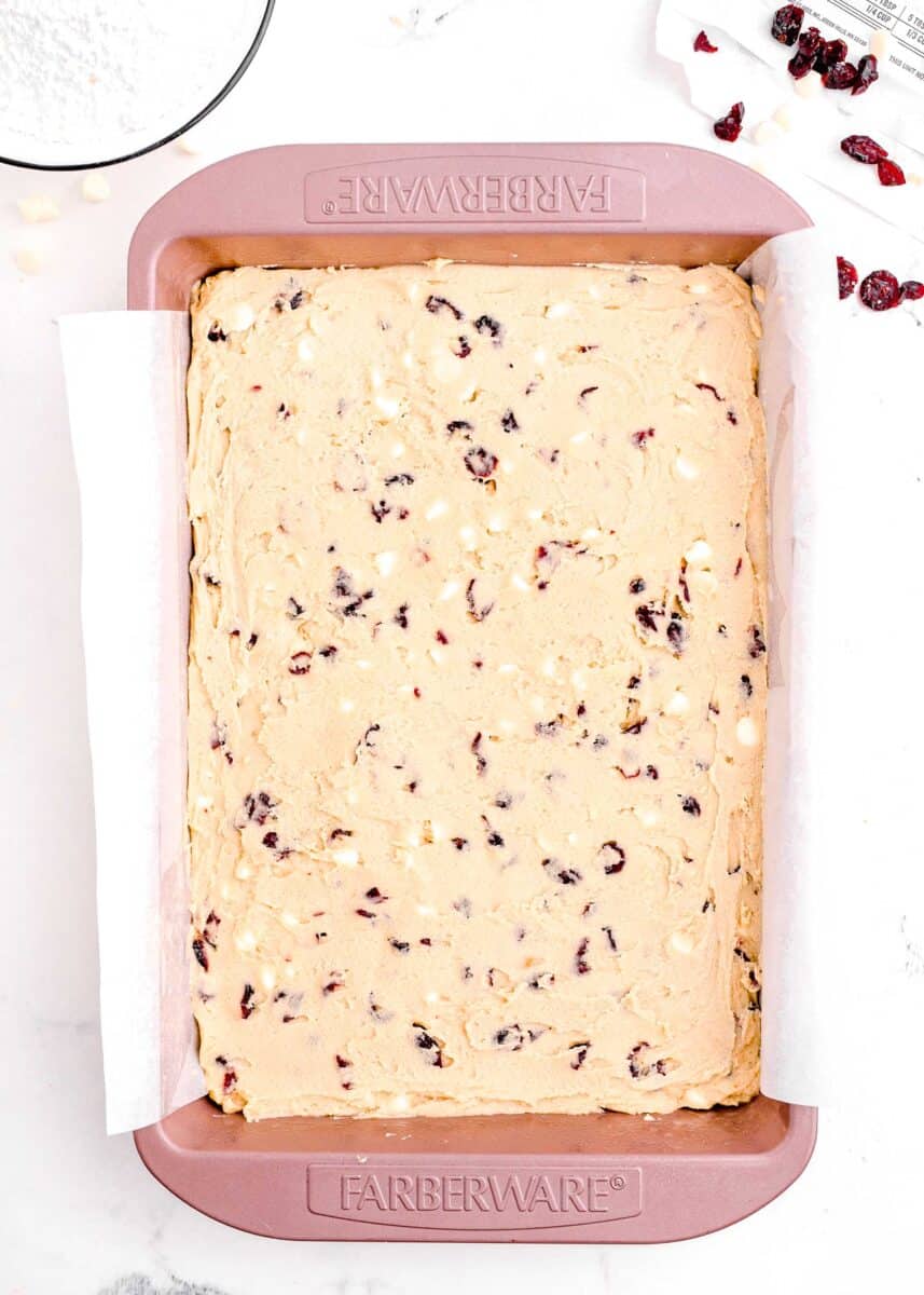 cranberry bliss bar dough spread evenly in a large pink baking sheet with parchment paper overhanging