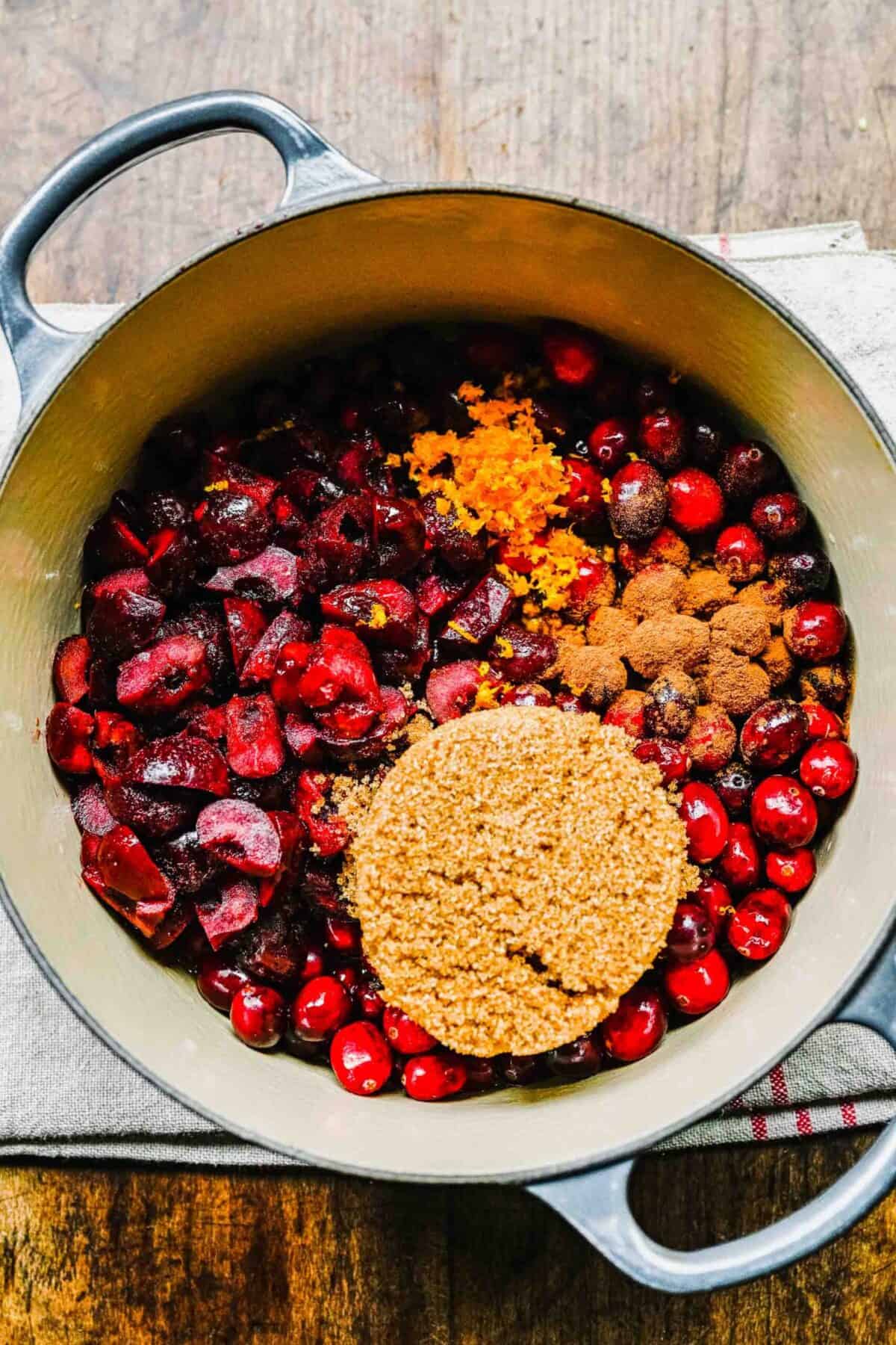 Cranberries and cherries in a pot, with brown sugar and orange zest on top