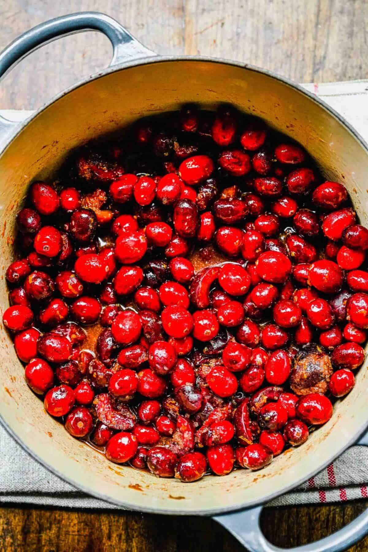 Cranberries and cherries cooking in a pot with brown sugar, orange juice, and orange zest