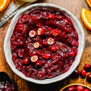 A bowl of cranberry cherry compote, topped with fresh cranberries, next to a bowl of cranberries and a bowl of cherries