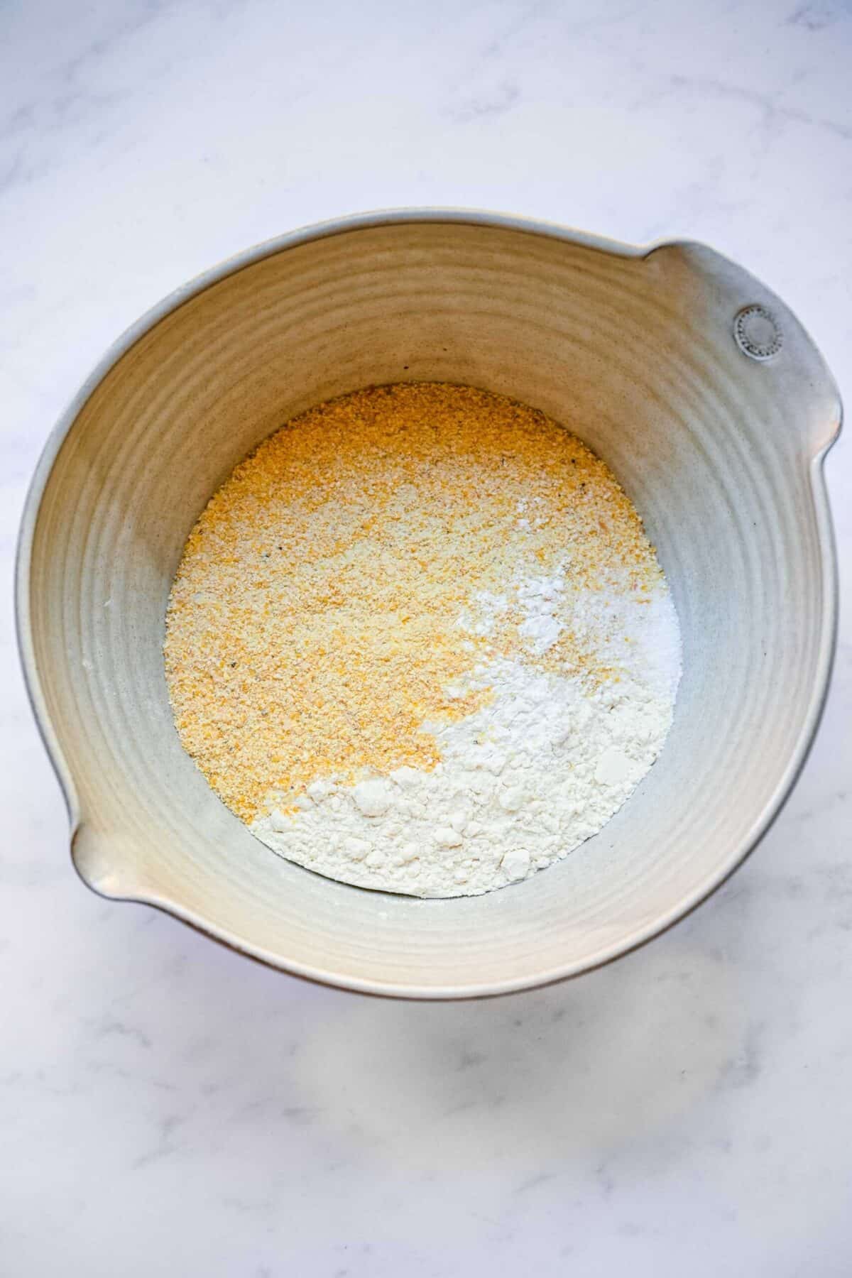 A mixing bowl with flour, cornmeal, baking powder, and salt