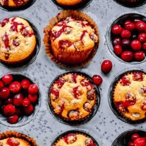 Overhead view of a muffin tin with cranberry cornbread muffins in some of the liners, and fresh cranberries in some of the other ones