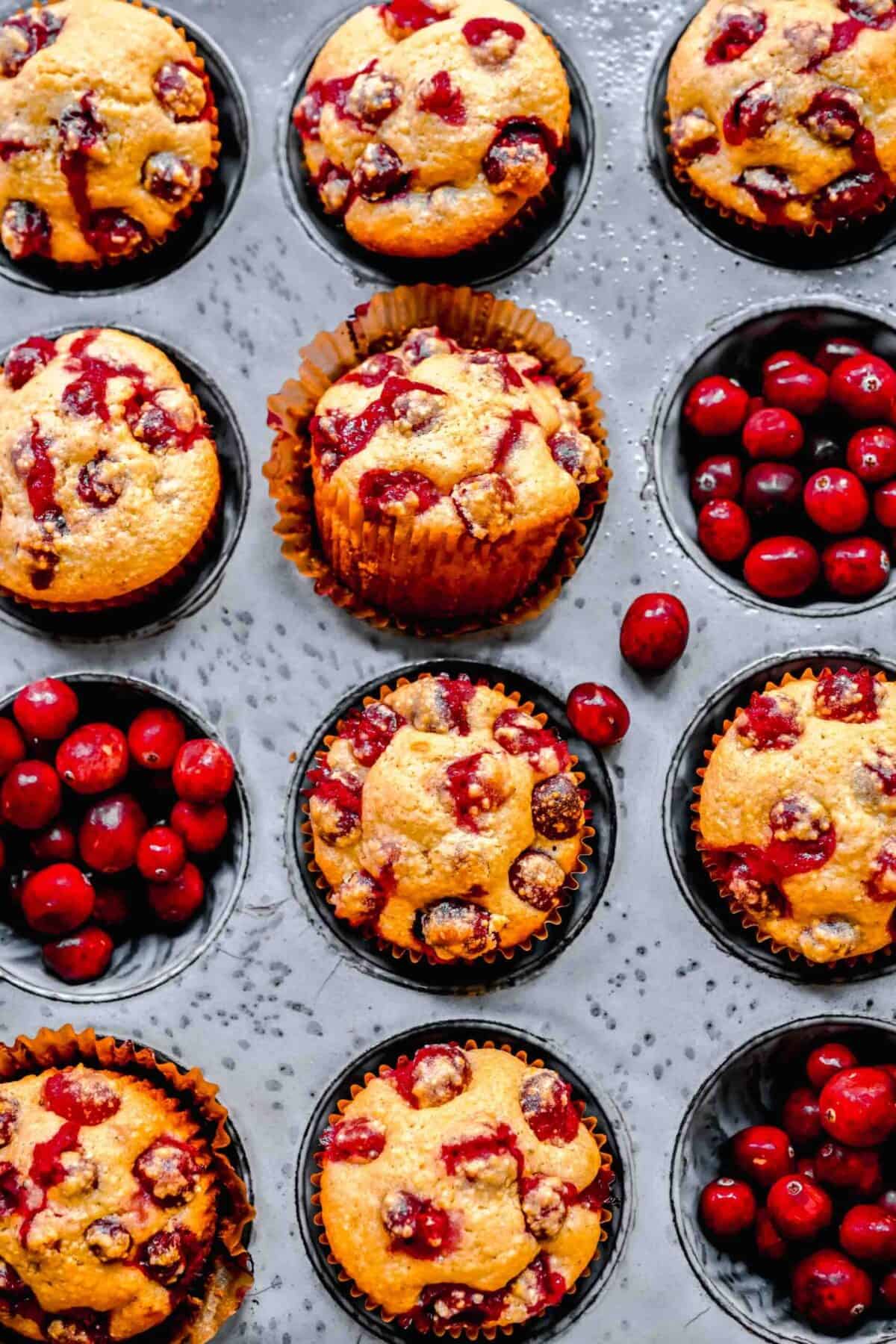 Overhead view of a muffin tin with cranberry cornbread muffins in some of the liners, and fresh cranberries in some of the other ones