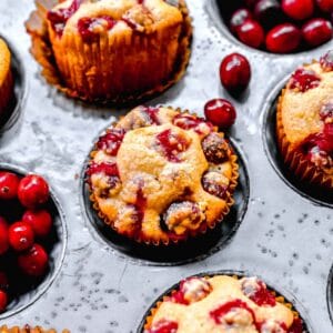 Close up of cranberry cornbread muffins in a muffin tin, surrounded by cranberries