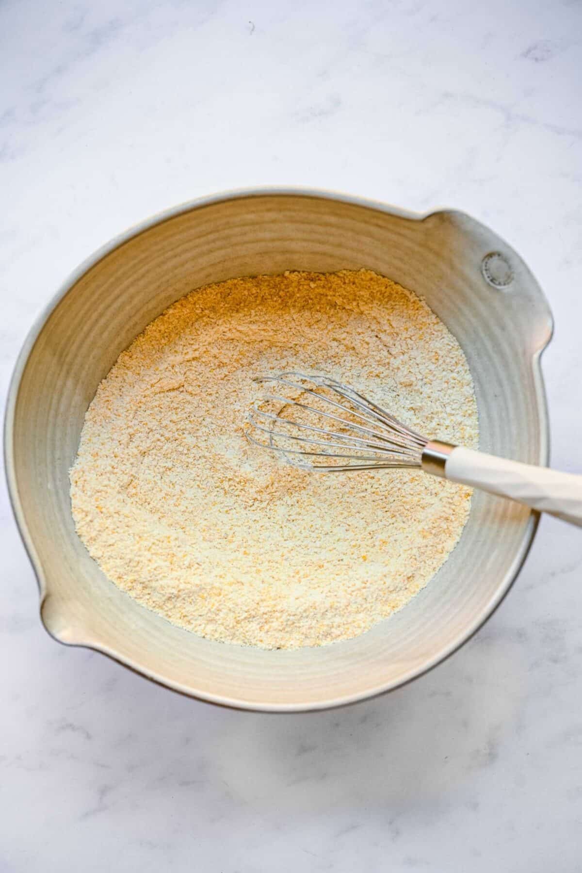 A mixing bowl filled with a cornmeal and flour mixture, with a whisk in it
