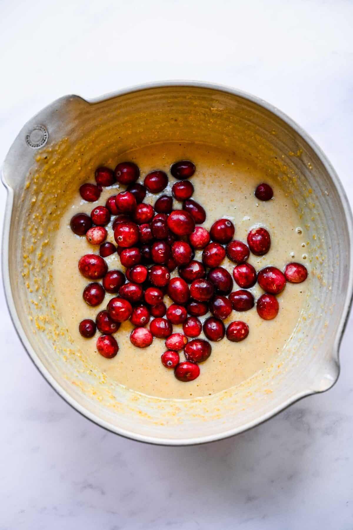 A mixing bowl filled with cornbread muffin batter, topped with fresh cranberries