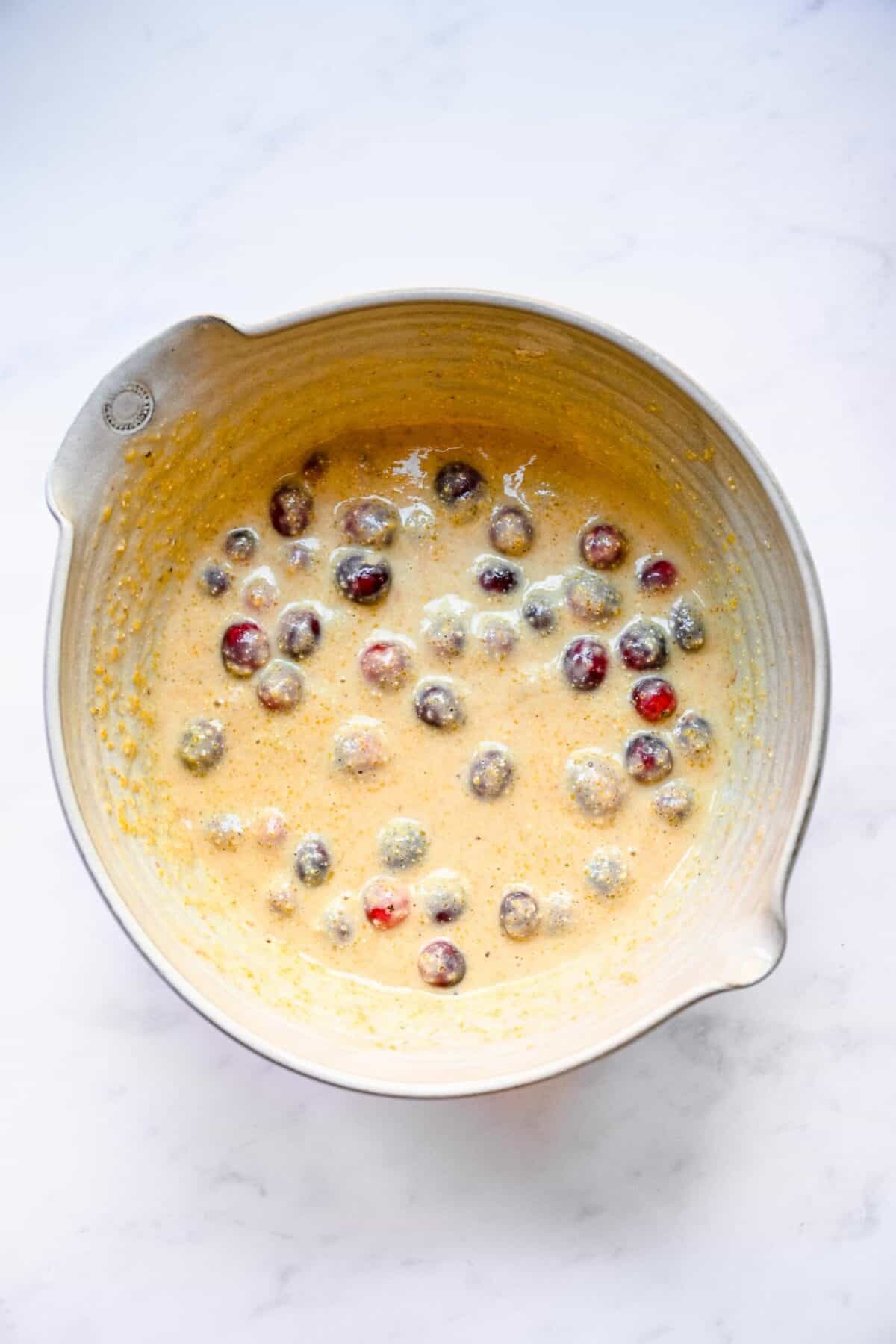 A mixing bowl filled with cornbread muffin batter, with cranberries folded in