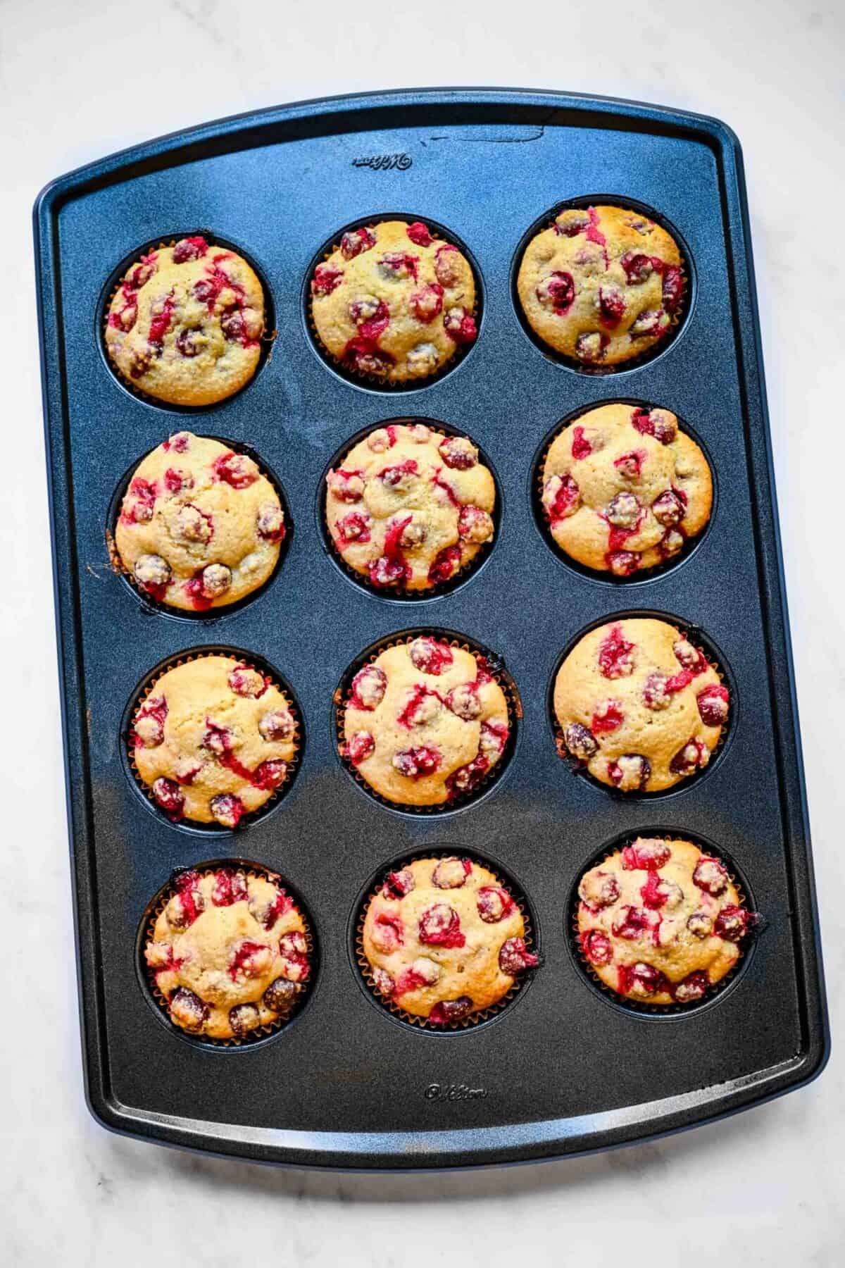 A muffin tin with 12 baked cranberry cornbread muffins in it