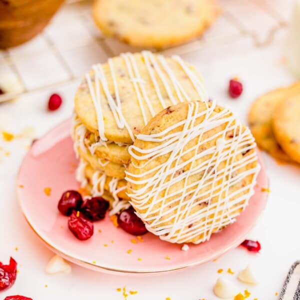 cranberry orange shortbread cookie on a pink plate with one cookie standing up to see the white chocolate drizzle detail