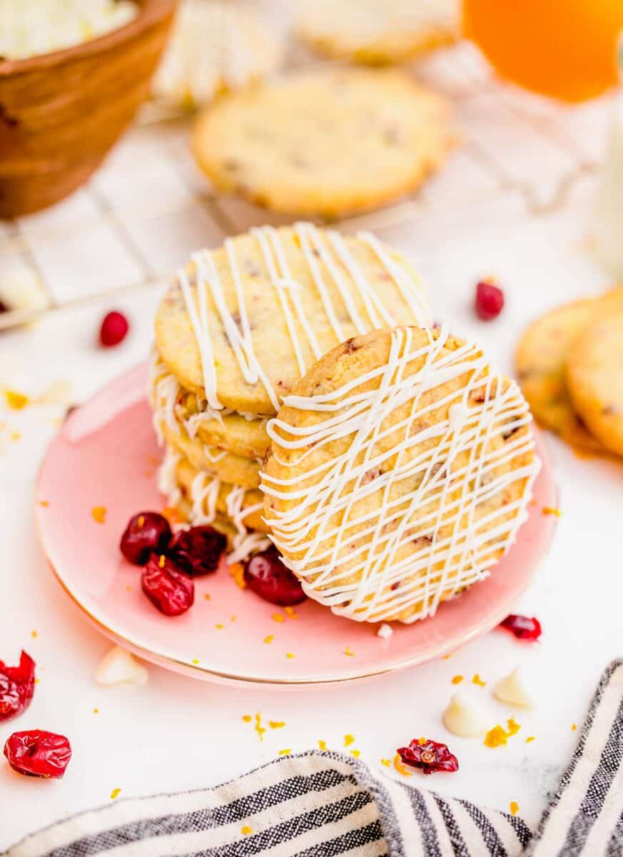 cranberry orange shortbread cookie on a pink plate with one cookie standing up to see the white chocolate drizzle detail