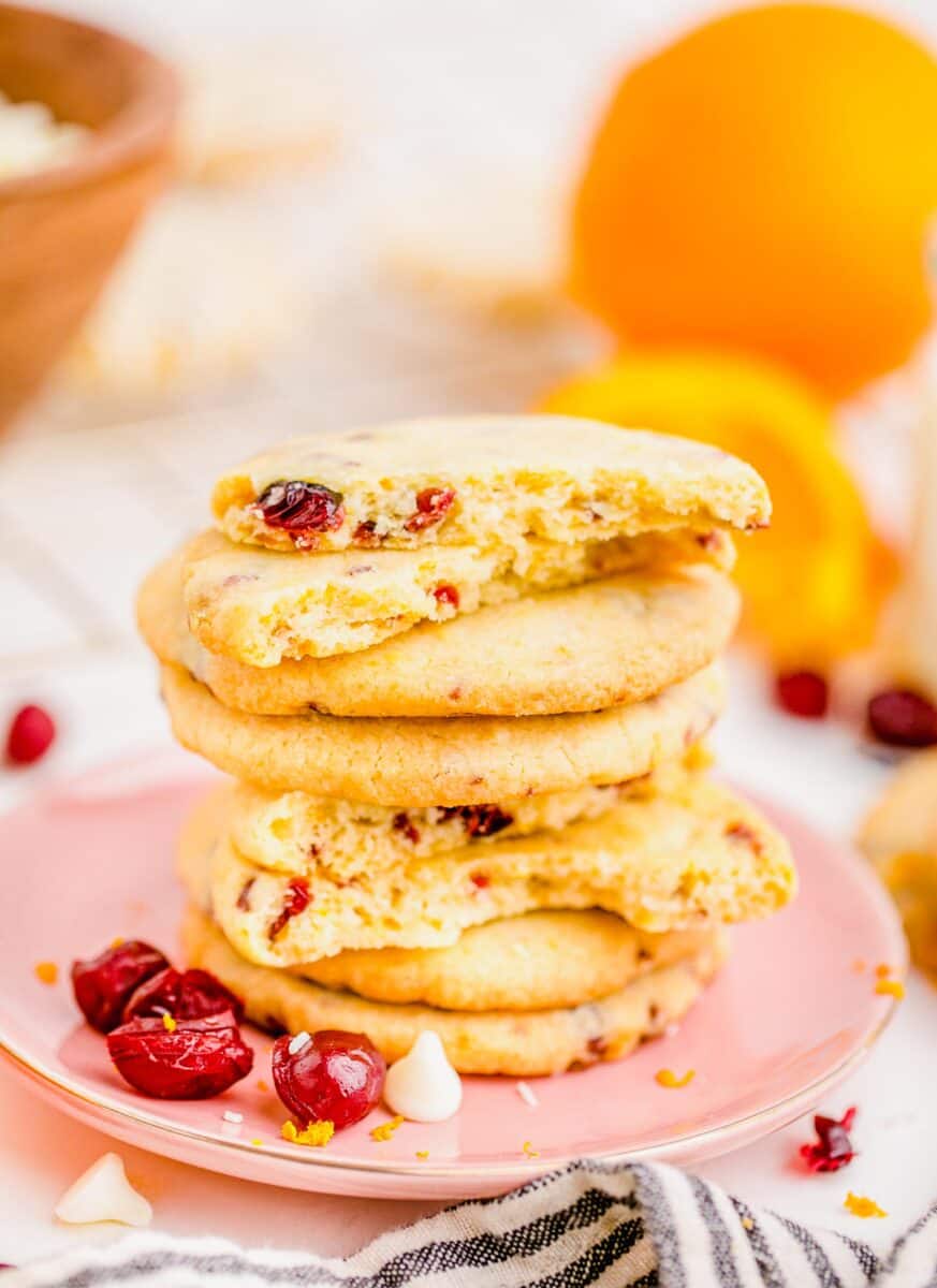 cranberry orange shortbread cookies stacked on top of a pink plate with dried cranberries and white chocolate chips on the plate