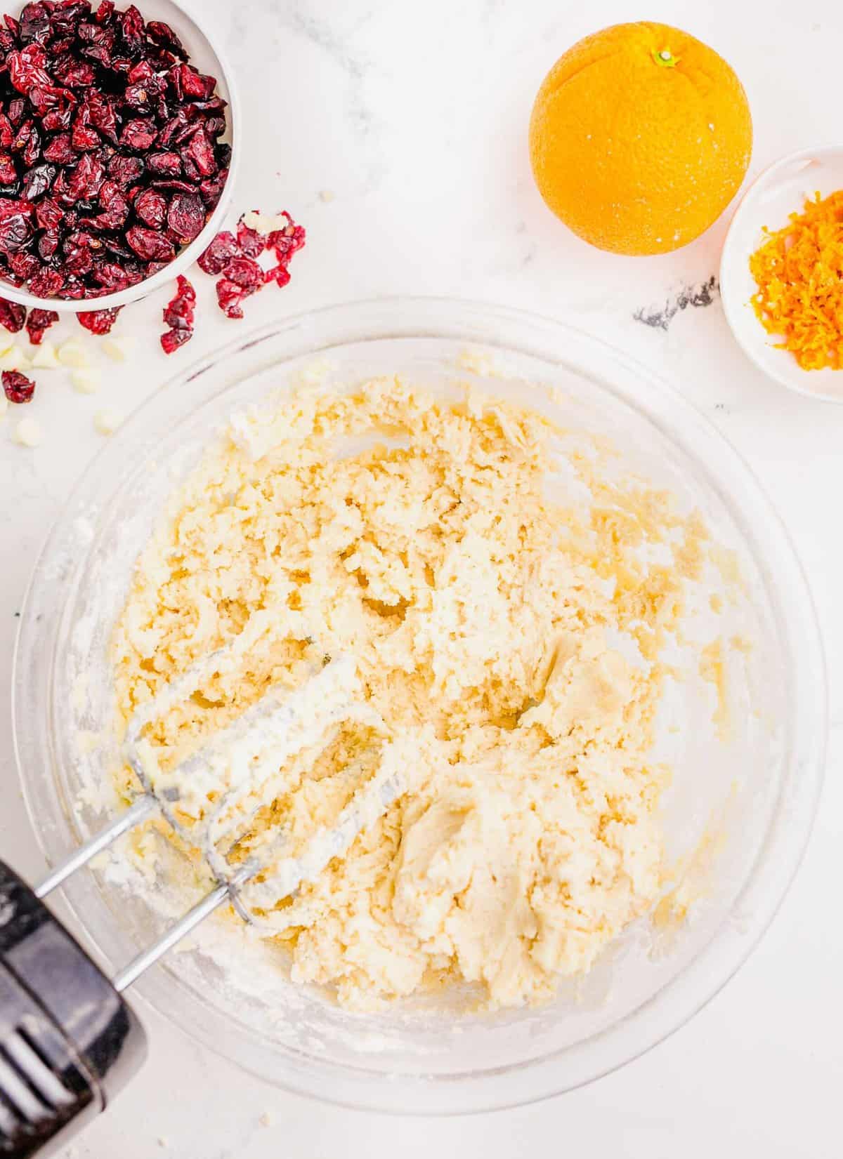 creaming together butter and sugar in a large clear bowl next to an orange and orange zest