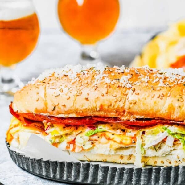A whole grinder sandwich on a tray, with two glasses of beer in the background