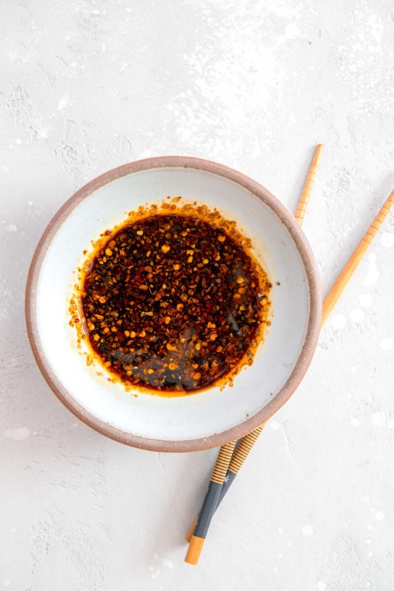 overhead image of dumpling sauce in a brown rimmed white ceramic bowl with wooden chopsticks next to the bowl