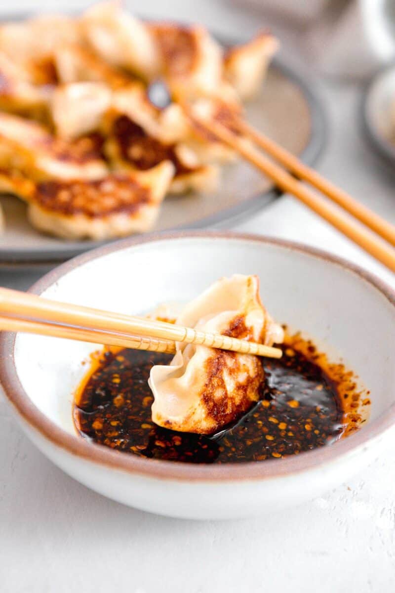 pan-fried dumpling being dipped into the dumpling sauce with wooden chopsticks