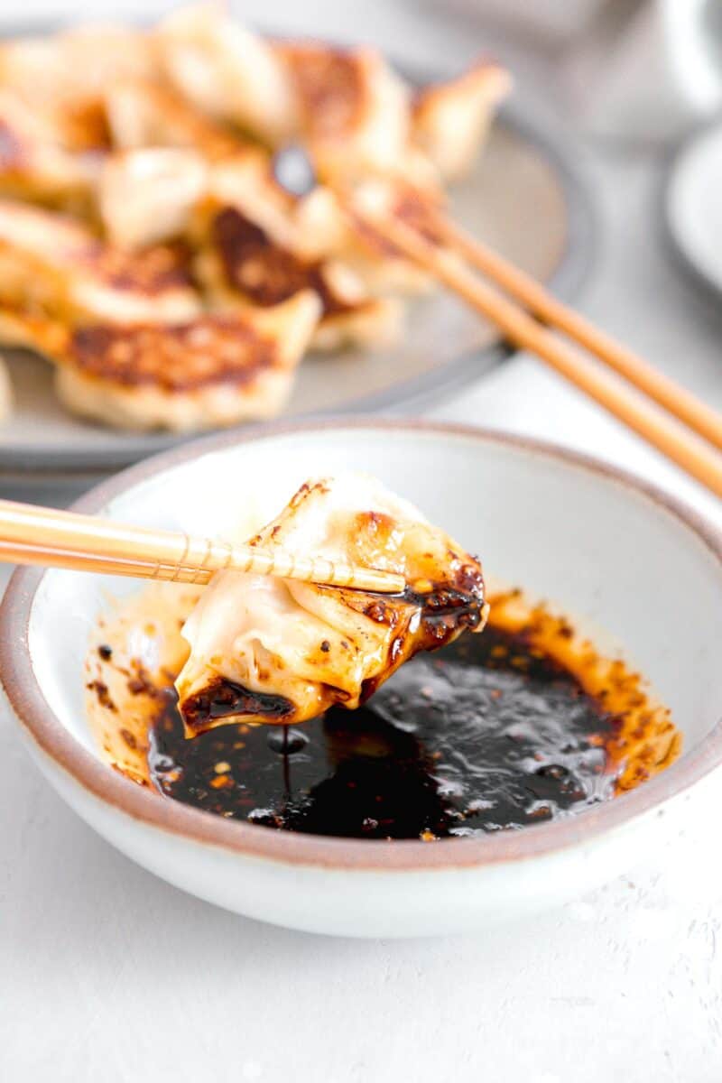 pan-fried dumpling being lifted out of the dumpling sauce after dipping with wooden chopsticks