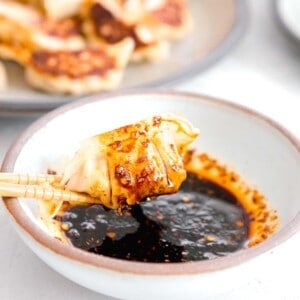 pan-fried dumpling dripping in dumpling sauce held onto by wooden chopsticks