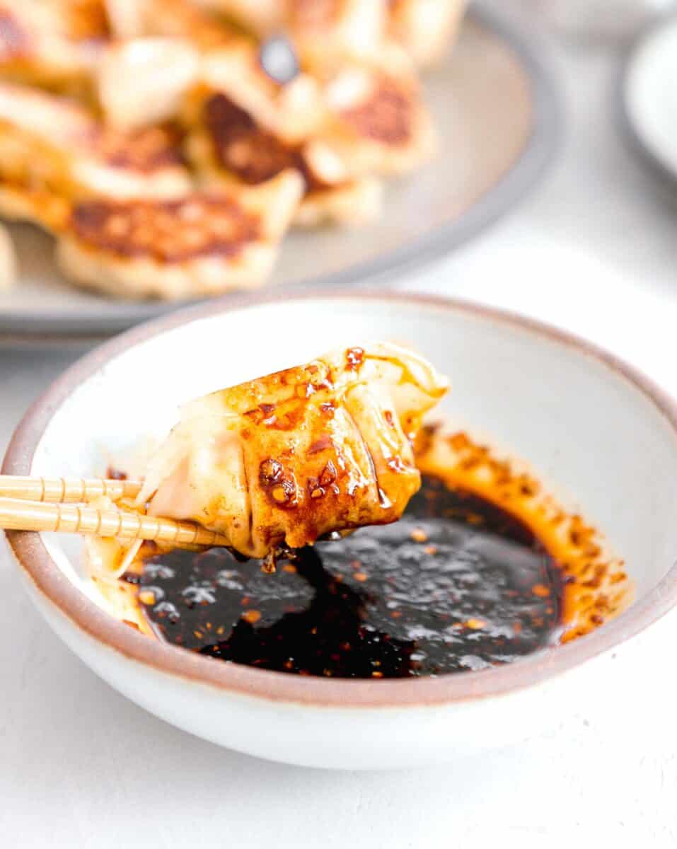 pan-fried dumpling dripping in dumpling sauce held onto by wooden chopsticks