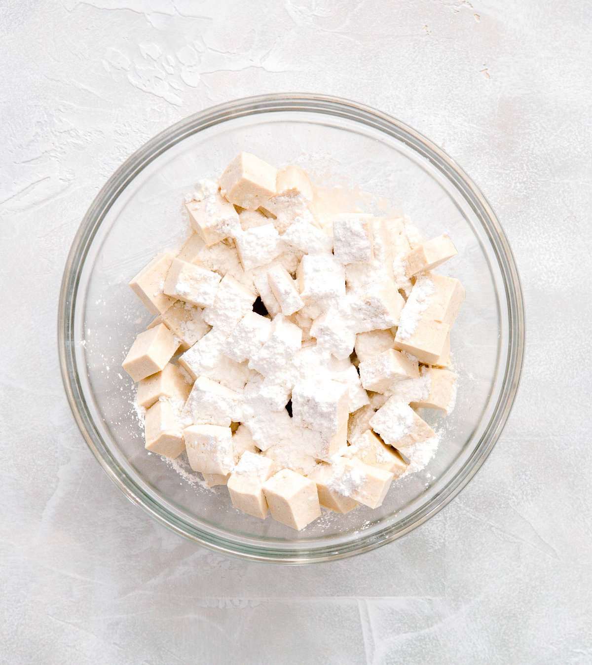 cubed tofu in a large clear bowl with cornstarch sprinkled on top