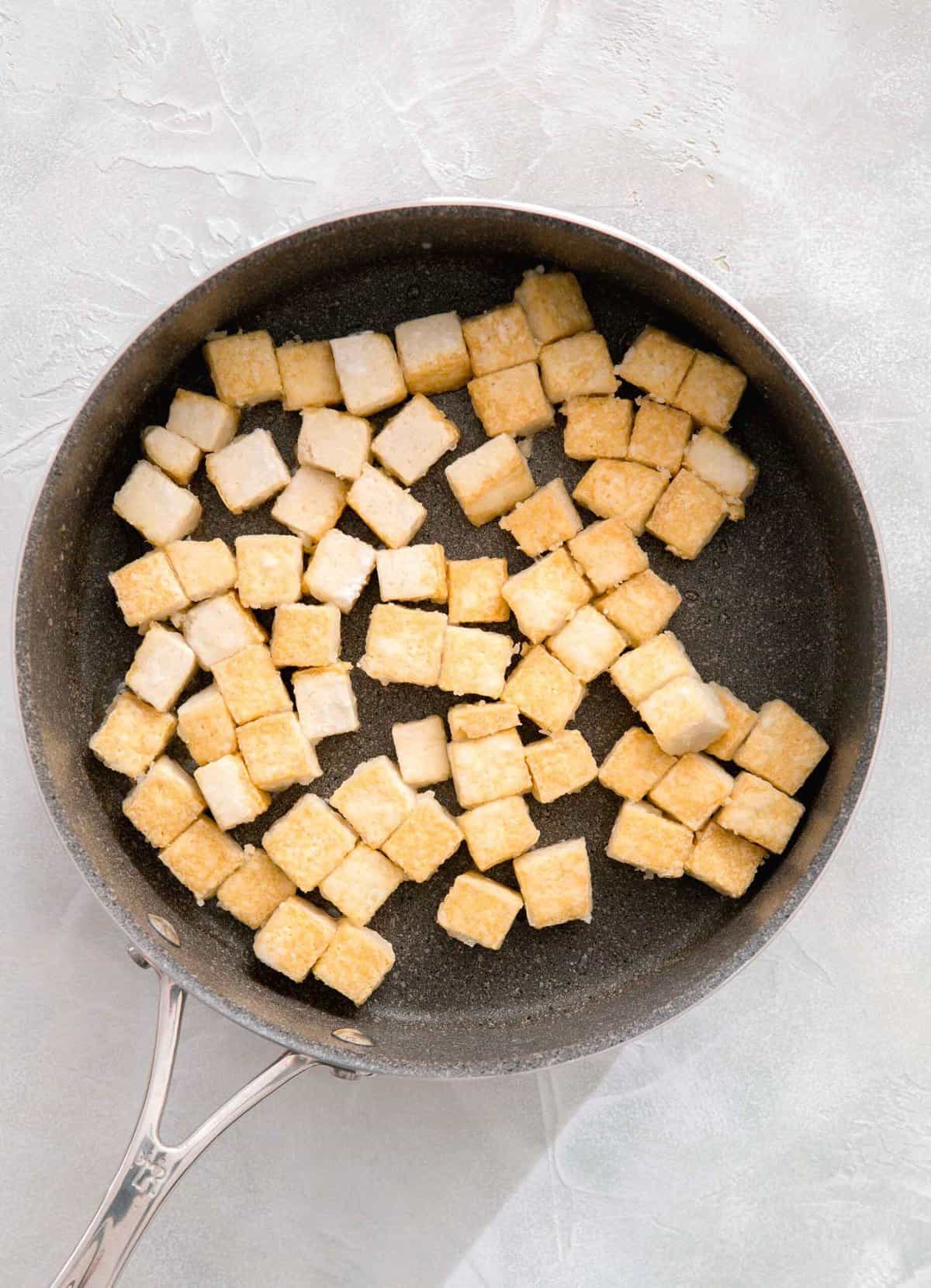 cubed tofu in a grey skillet being cooked and exterior is crispy