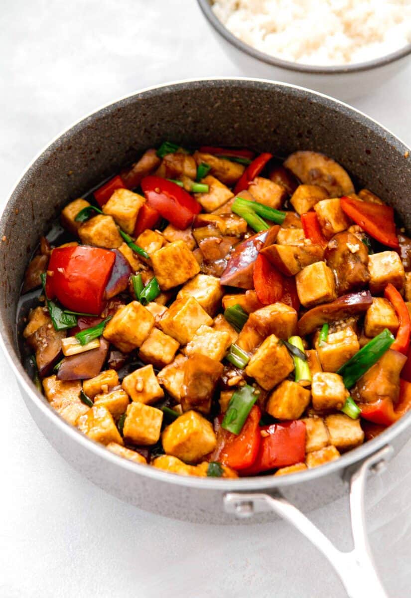 image of eggplant tofu recipe in the skillet with brown sauce coating the ingredients. a bowl of white rice can be seen next to the skillet