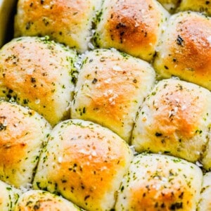 Close up of garlic herb parker house rolls in a pan, topped with garlic and herbs