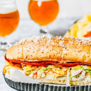 A whole grinder sandwich on a tray, with two glasses of beer in the background