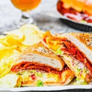 Close up of a grinder sandwich cut in half, with a beer and a sandwich in the background
