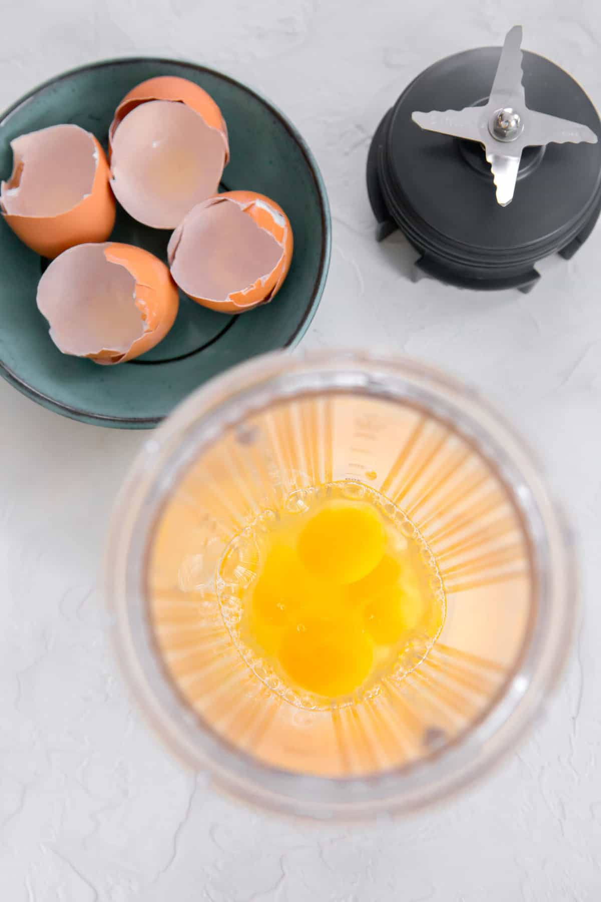 overhead shot of eggs in a blender jar next to egg shells and blender blade