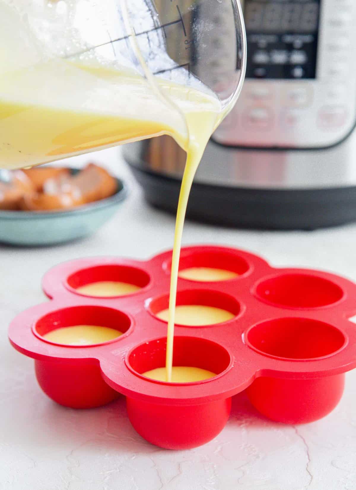 egg mixture in a clear container being poured into a red egg mold in front of an instant pot and blue plate with egg shells