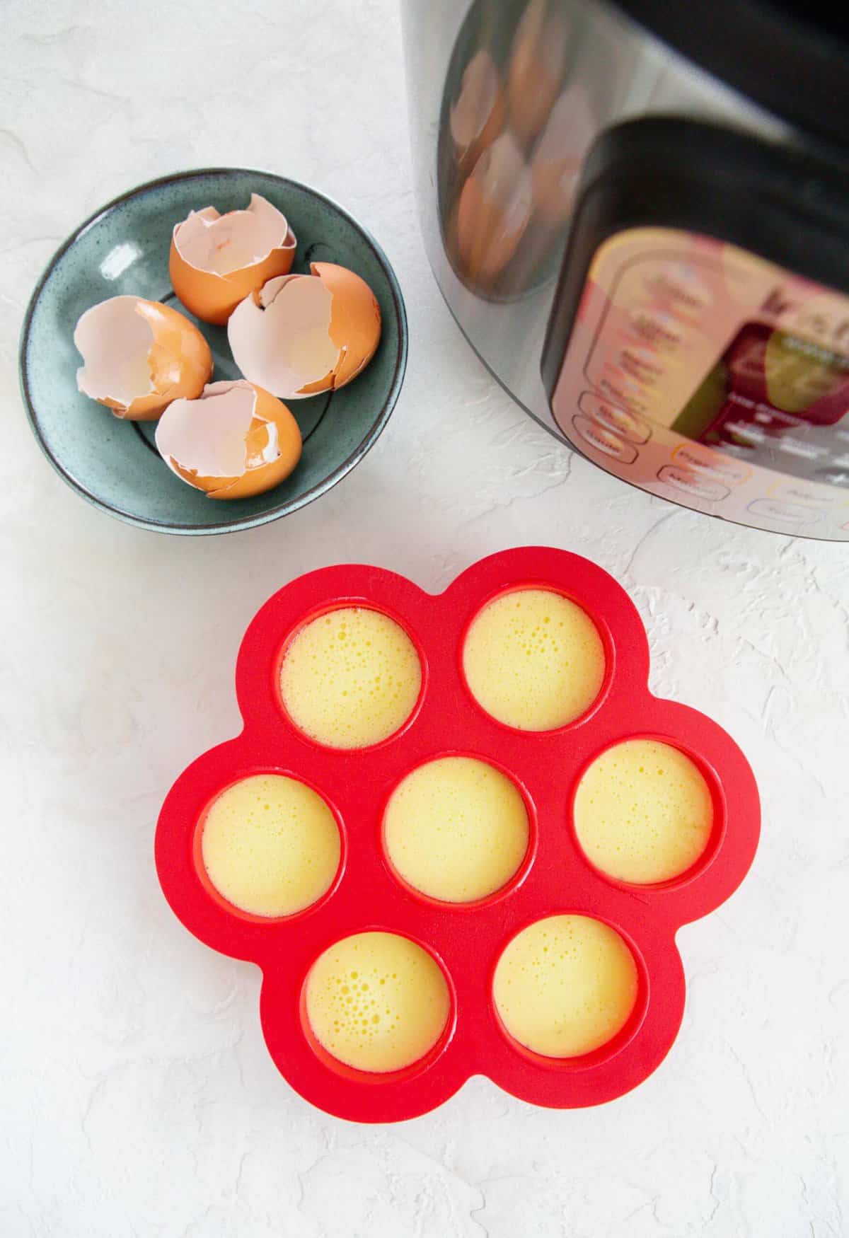 overhead shot with filled red egg molds next to a blue plate with egg shells and an instant pot