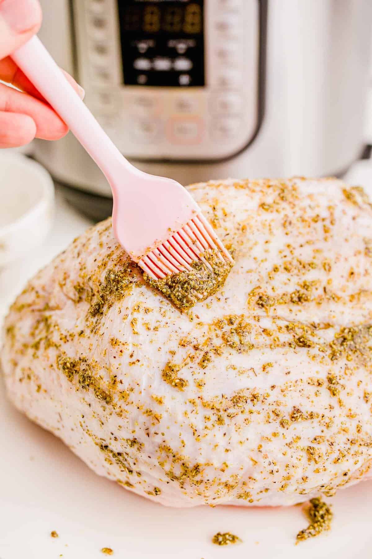 brushing spice mixture with a pink silicone brush evenly on turkey breast