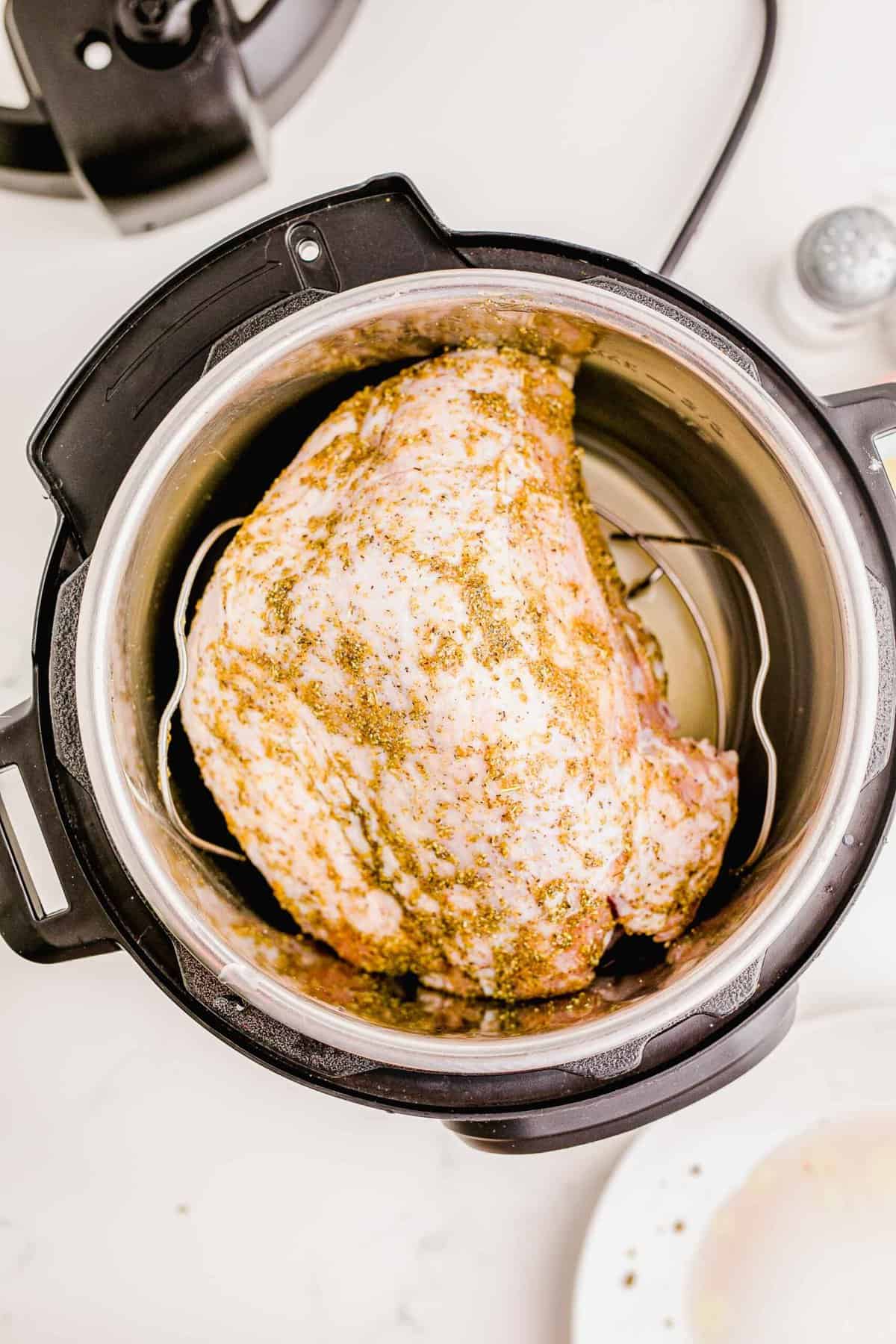 overhead image of seasoned turkey breast on top of the metal rack in the insert of an instant pot