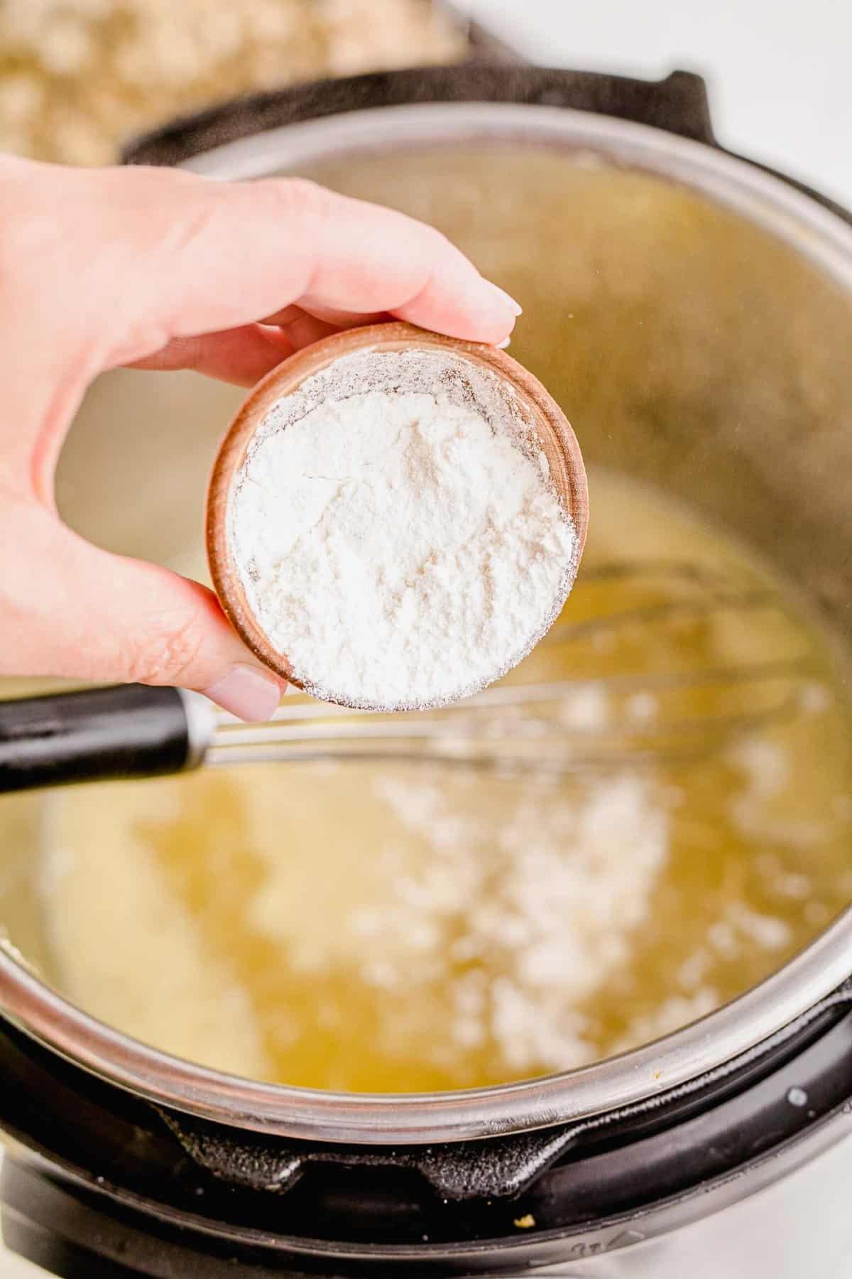 sprinkling flour into the turkey drippings mixture with the instant pot in the background