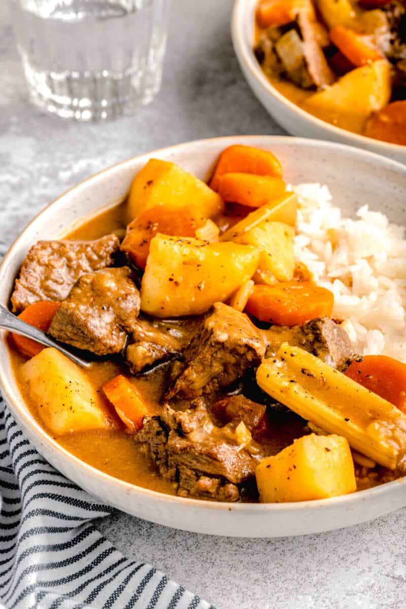 beef, potatoes, celery, and carrots in a stew-like sauce on a bed of white rice in a rimmed ceramic bowl