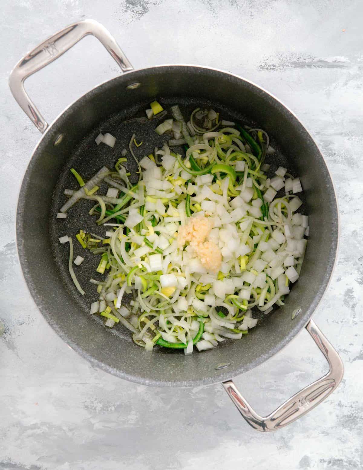 leeks, onions, and garlic added into a pot to saute