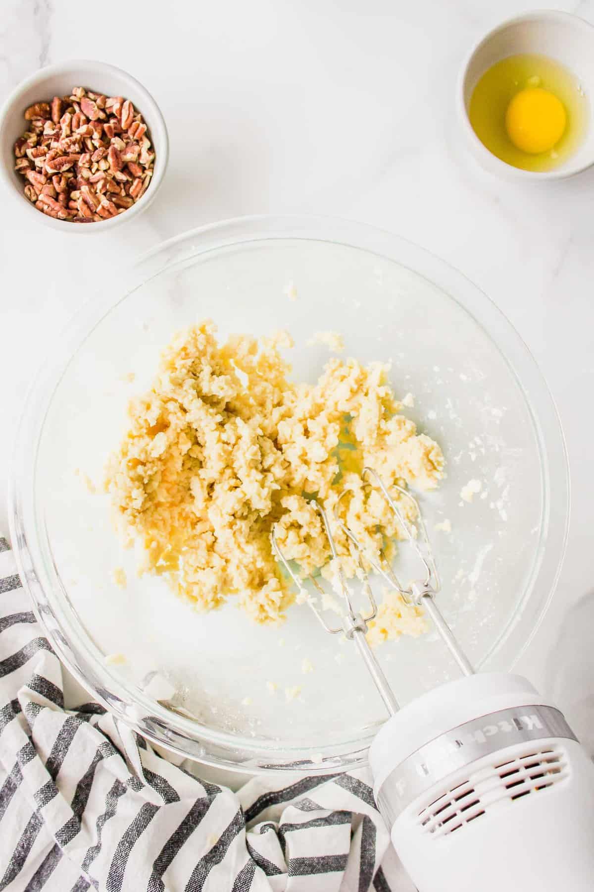 creaming cream cheese, butter, and flour together in a clear bowl with a hand mixer next to a striped linen towel