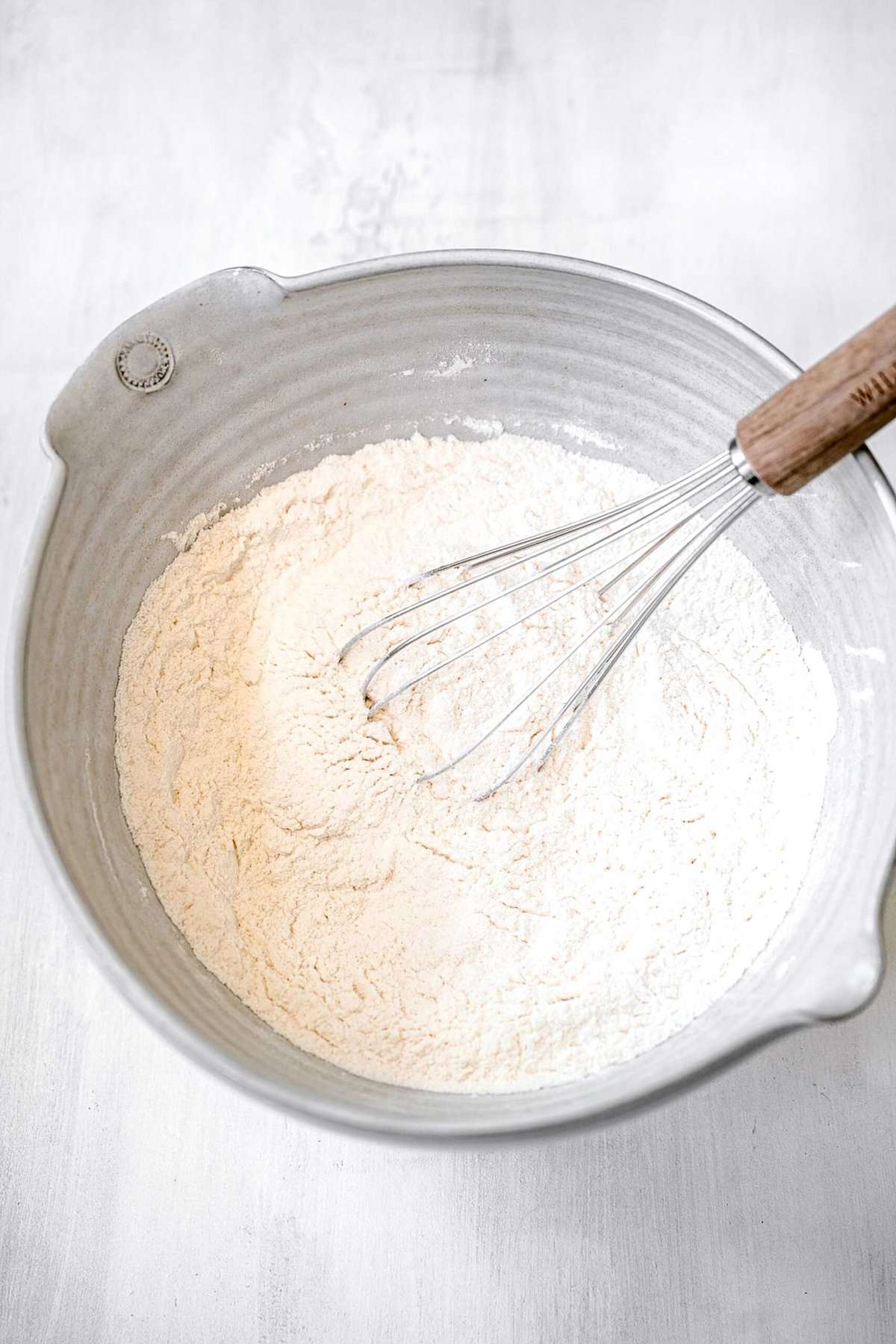 whisking the dry ingredients together in a large grey bowl with a spout