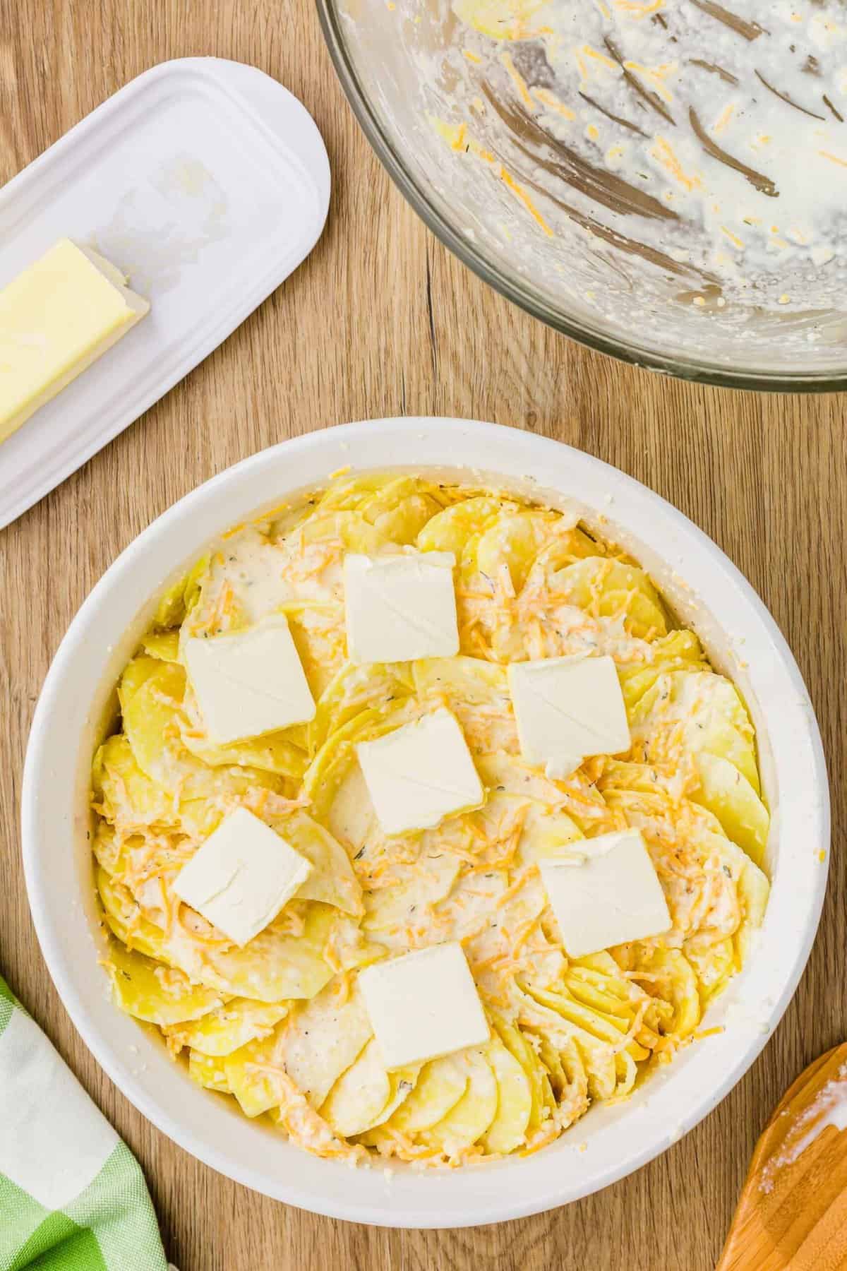 thinly sliced potatoes layered in a baking dish with pads of butter slices on top