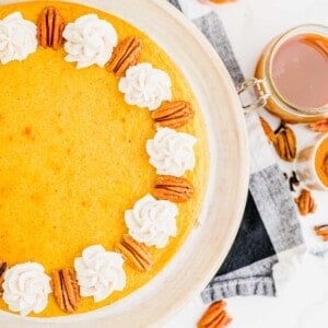 Partial view of a pumpkin cheesecake, topped with dollops of whipped cream and pecans