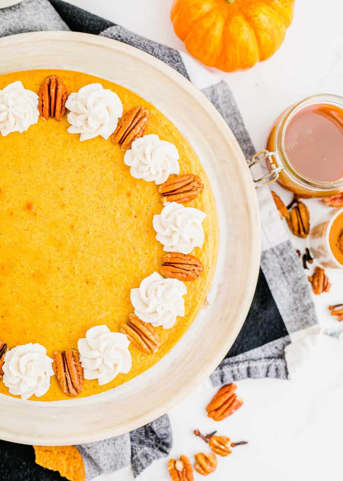 Partial view of a pumpkin cheesecake, topped with dollops of whipped cream and pecans