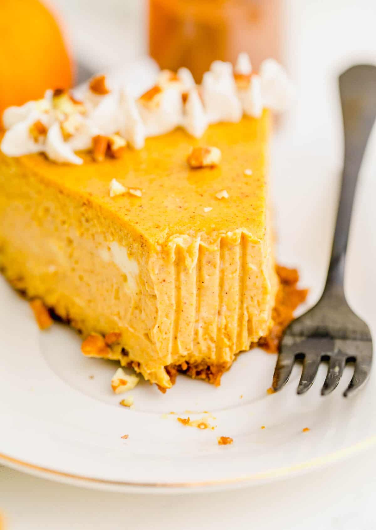 Close up of a slice of pumpkin cheesecake with a bite taken out of it, with a fork next to the cake