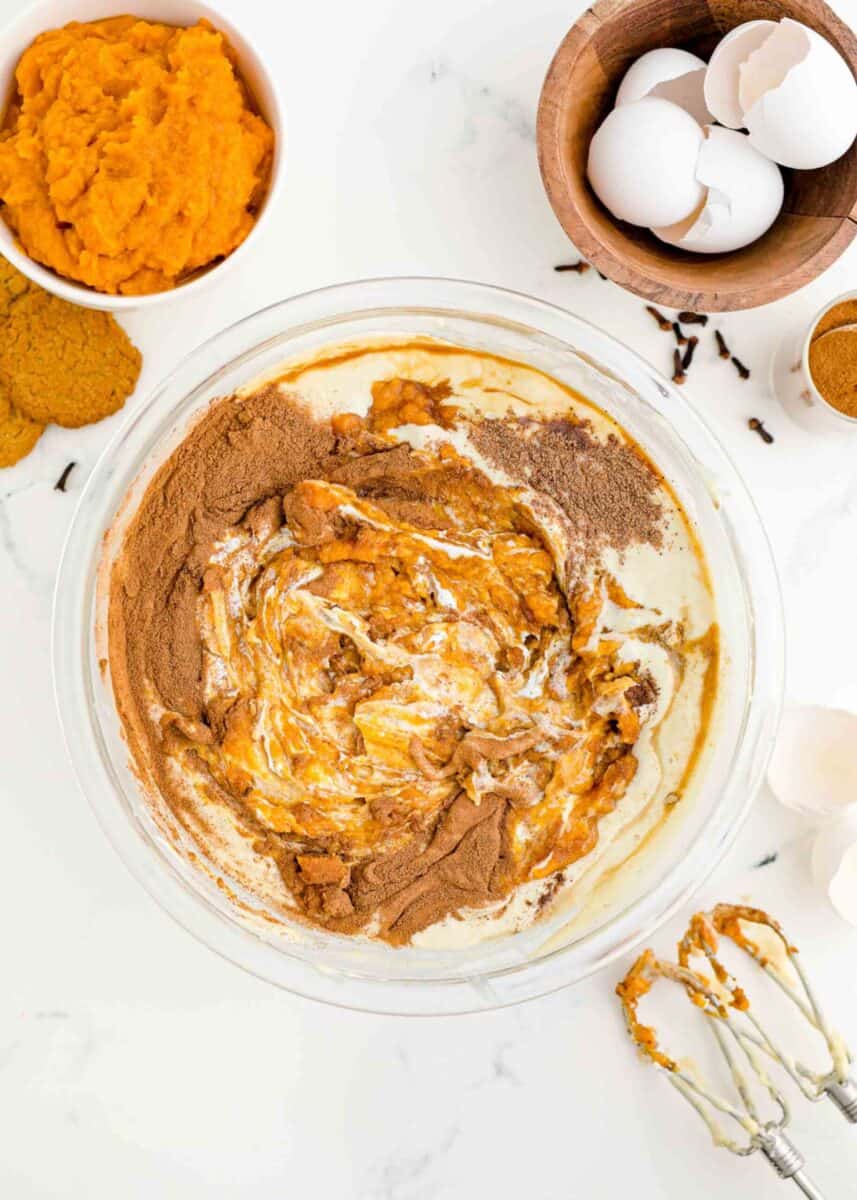 A mixing bowl with the ingredients for pumpkin cheesecake filling being mixed together