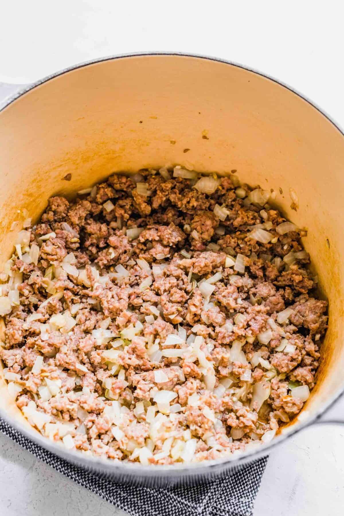 A pot with cooked, broken up sausage in it, as well as onions