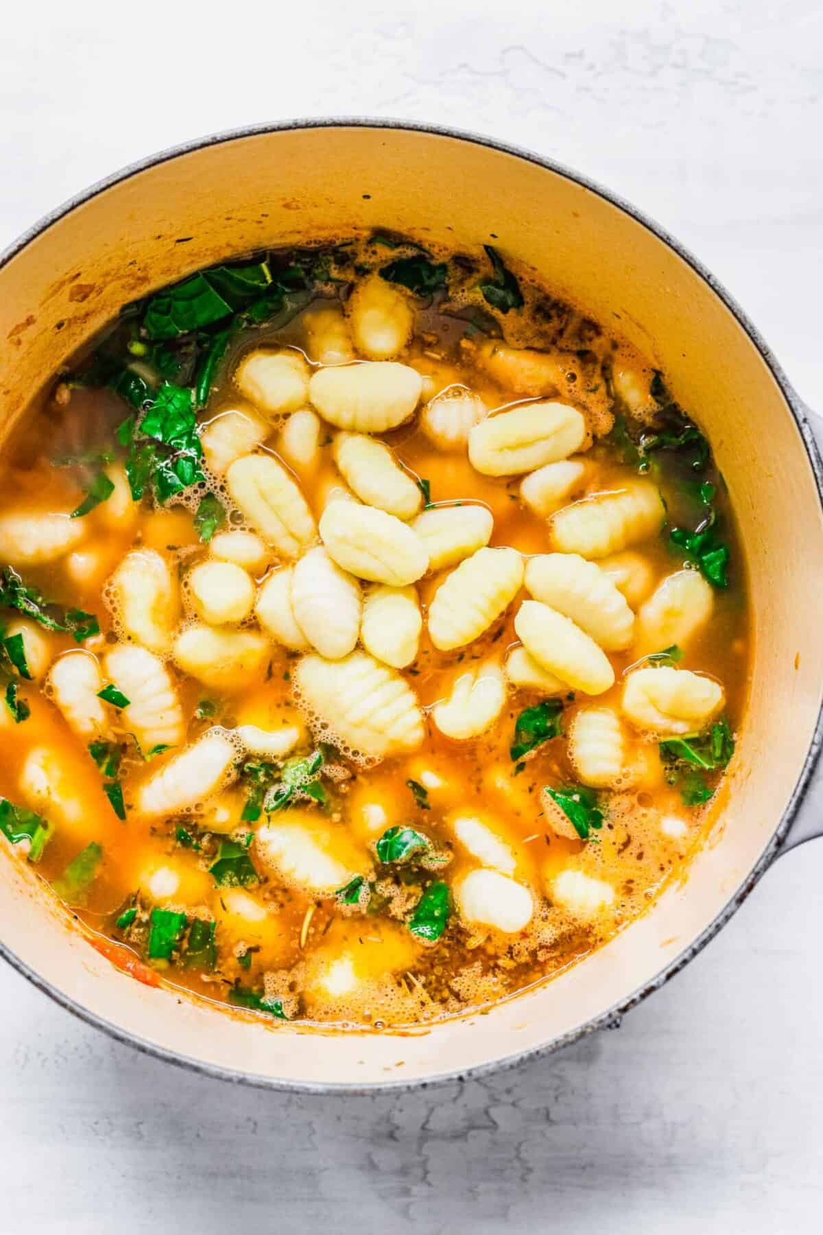 A pot of soup with gnocchi and kale added on top of it